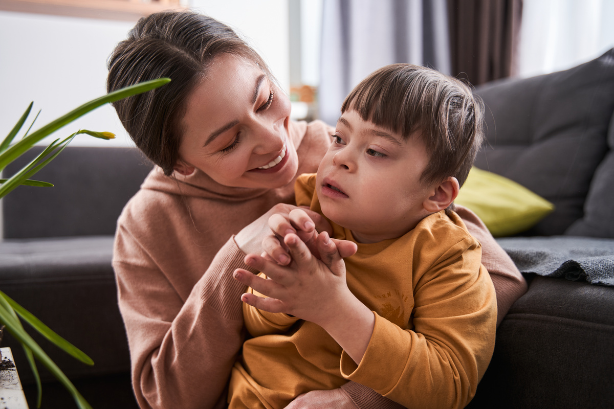 Caucasian woman bonding to her son with genetic disorder while sitting near the sofa