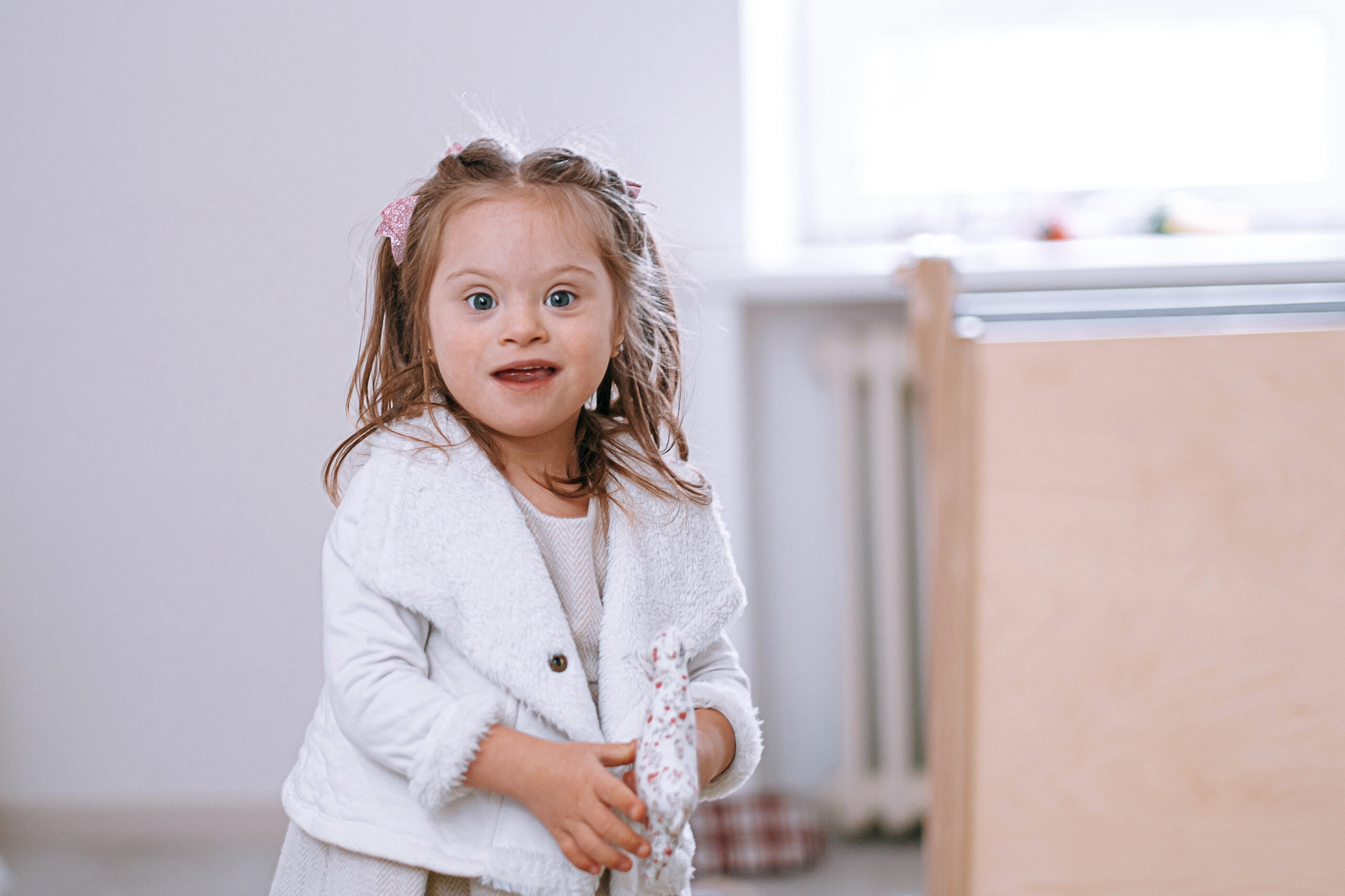 child girl with down syndrome with a toy in her hands looking happily at the camera