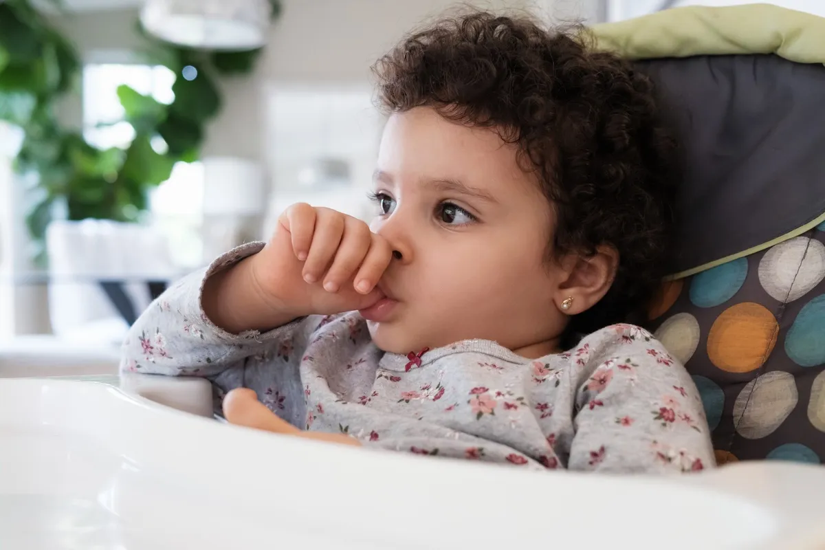 Cute two year old baby girl sitting on a high chair sucking her thumb in a home setting