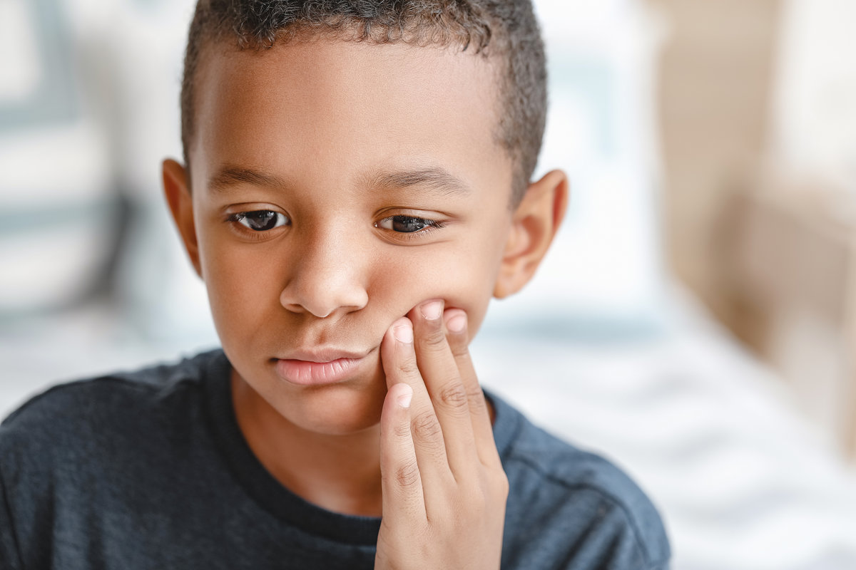 Little African-American boy suffering from toothache at home