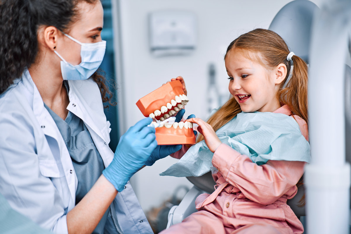 Children's dentistry. Cropped image of child and nurse holding mockup of jaw and talking about brushing teeth to child. First visit to the dentist.