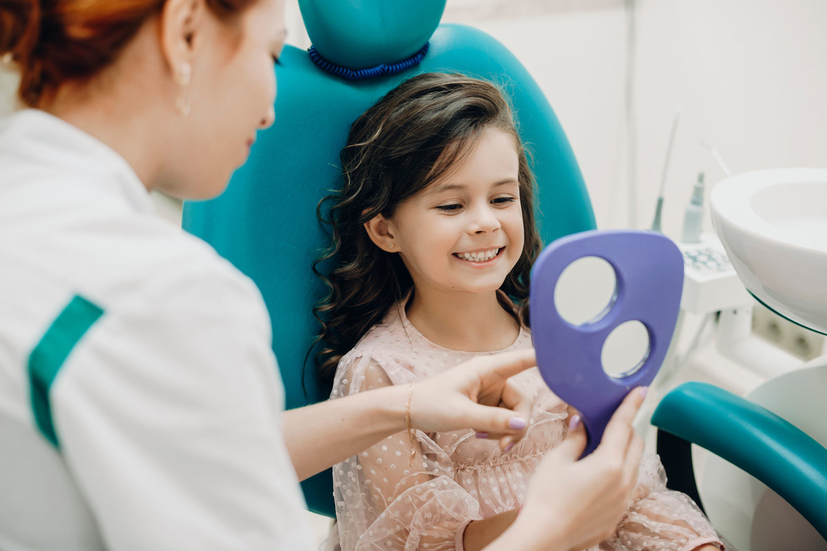 Close up portrait of a lovely little girl looking in the mirror at the dentist after examination. Smiling little kid smiling at stomatology examination.