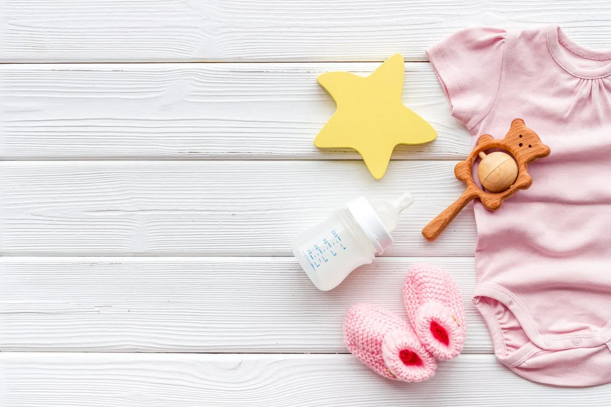 Baby background - pink color. Clothes, booties and accessories for newborn girl on white wooden table top-down frame copy space
