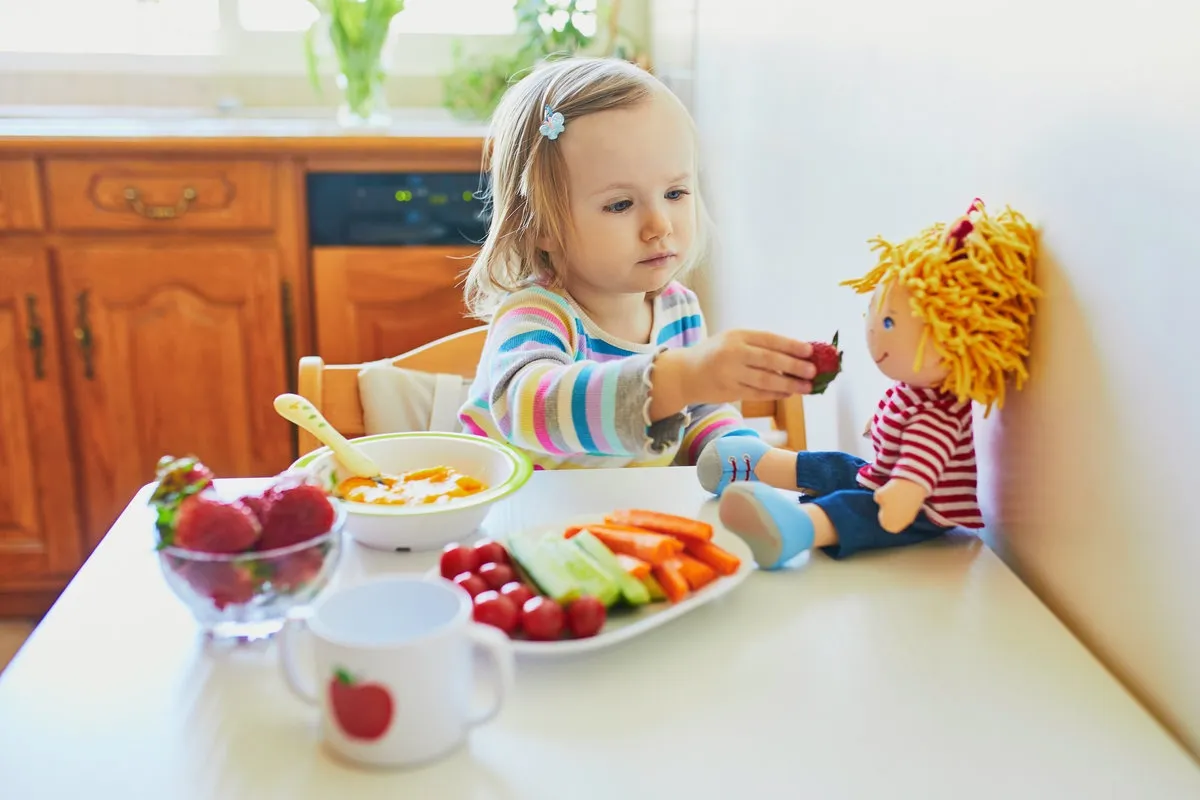 Adorable toddler girl eating fresh fruits and vegetables for lunch
