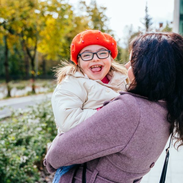 Cute little girl in a red beret with special needs enjoy having fun spending time with mother outdoor in aututm time. Happy family moments concept.
